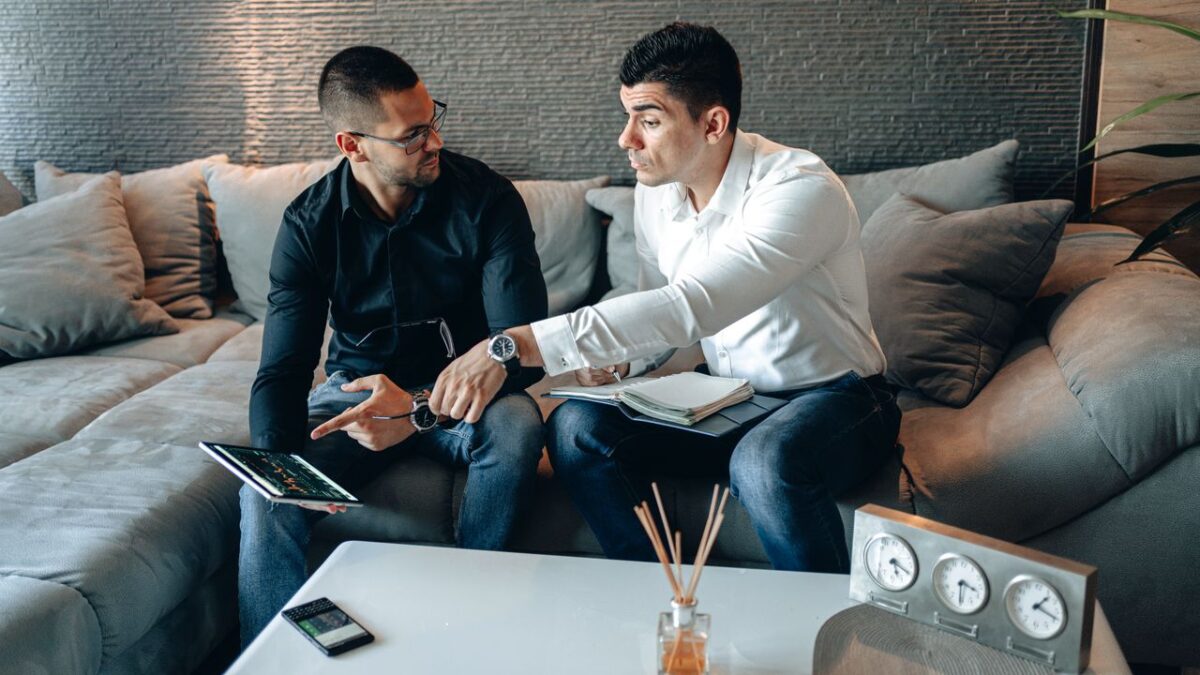 about-us-01 Two men discussing business ideas on a sofa using a tablet in a cozy home office setting.